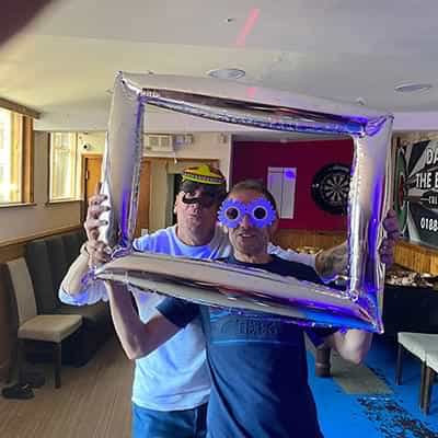Ryan's Dad, Nigel and Dave wearing funny faces behind a blow-up picture frame
